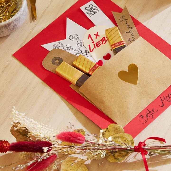 Gebastelte Karte mit aufgeklebtem Umschlag. Darin stecken merci Schokoladen-Stäbchen. Darunter steht in Handschrift: Beste Mama
